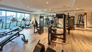 Un gimnasio espacioso con diversos equipos de ejercicio, ventanas amplias y suelo de madera.