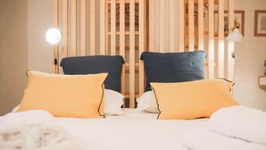 A hotel room with two beds, each with yellow pillows, a wooden partition, and a round table with a lamp. - GRABBIA 1 by Deign Studio (Bellano)