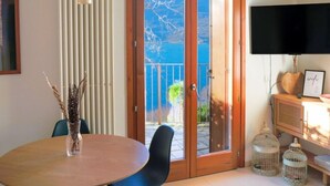 A room with a round table, chairs, a radiator, a TV, and a view through a glass door. - GRABBIA 1 by Deign Studio (Bellano)