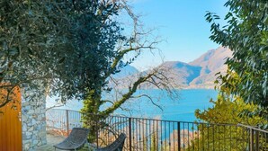 A patio with two chairs, a stone wall, and a view of a lake and mountains. - GRABBIA 1 by Deign Studio (Bellano)