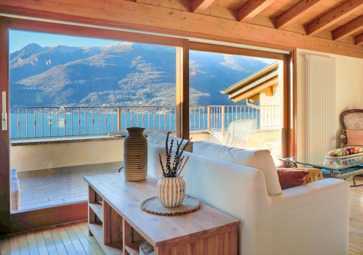 Ein Balkon mit Blick auf Berge und einen See, ein weißes Sofa und ein Holztisch mit einer Vase.