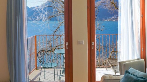 Habitación con balcón y vistas a un paisaje montañoso y una masa de agua.