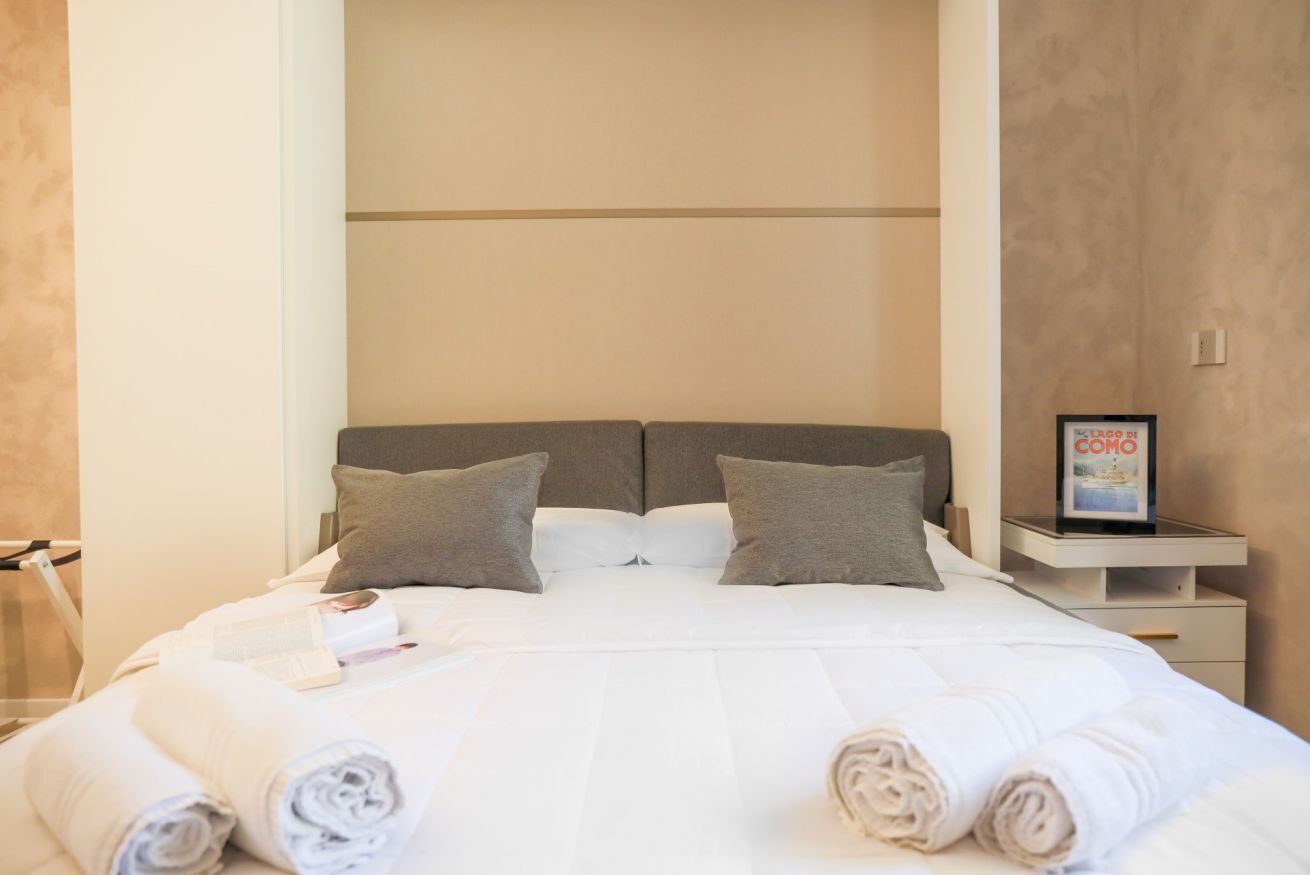 A neatly made bed with pillows, a bedside table with a framed picture, and a towel on the floor.