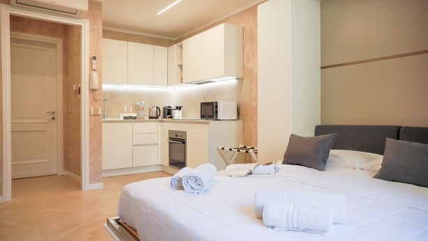A modern hotel room with a neatly made bed, a small kitchenette, and a separate bathroom. - BLUE WAVE by Design Studio (Bellano)