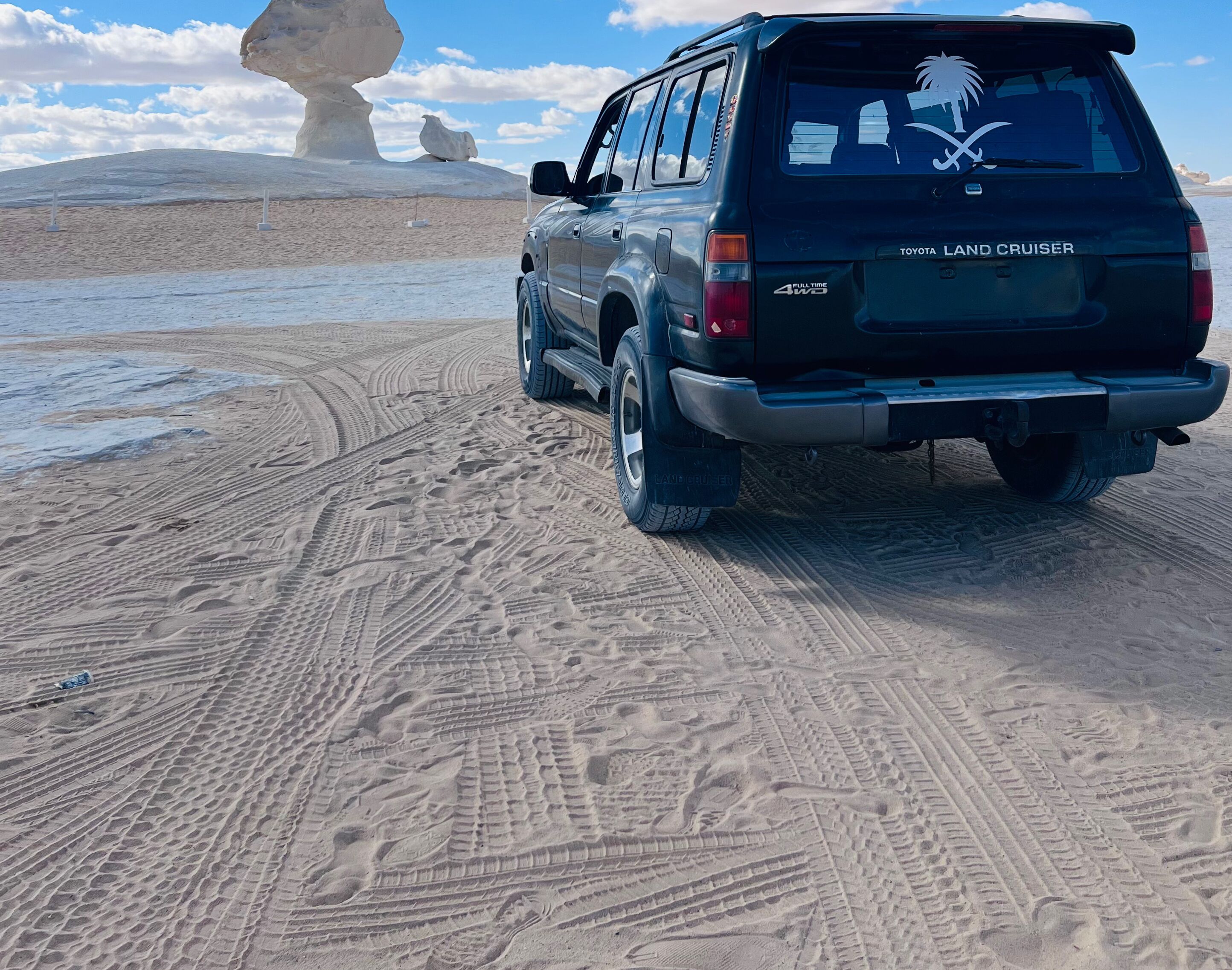 Un Toyota Land Cruiser est garé sur une plage de sable, et on peut voir les traces de pneus.