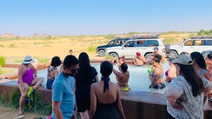 A group of people gathered around a swimming pool with a vehicle in the background. - White Desert Camp Safari (Al Bawiti)
