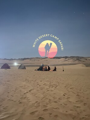 Ein Lager in der Wüste mit Zelten und einer Gruppe von Menschen, die sich um ein Lagerfeuer versammelt haben.