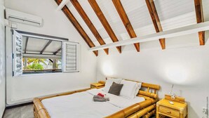 Ein Zimmer mit einem Bambusbett, einem Fenster mit Fensterläden, einem Nachttisch und einer wandmontierten Klimaanlage.