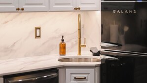 Eine Küche mit weißen Schränken, einem schwarzen Kühlschrank und einem goldenen Wasserhahn.