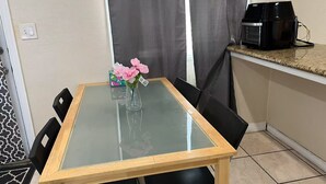 A small dining area with a glass-top table, black chairs, a vase with flowers, a coffee maker, and a patterned rug. - Spacious 4-bedroom villa in charming West Covina with AC, WiFi (West Covina)