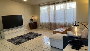 A living room with a flat-screen TV, a coffee table, a sofa, and a lamp. - Spacious 4-bedroom villa in charming West Covina with AC, WiFi (West Covina)