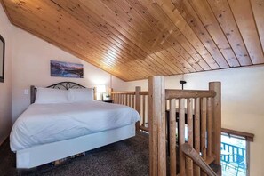 Un dormitorio con techo de madera, una cama, un cuadro en la pared y una escalera.