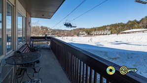 Ein überdachter Balkon mit Metallstühlen und einem Tisch, mit Blick auf eine verschneite Landschaft, im Hintergrund ist eine Seilbahn zu sehen.
