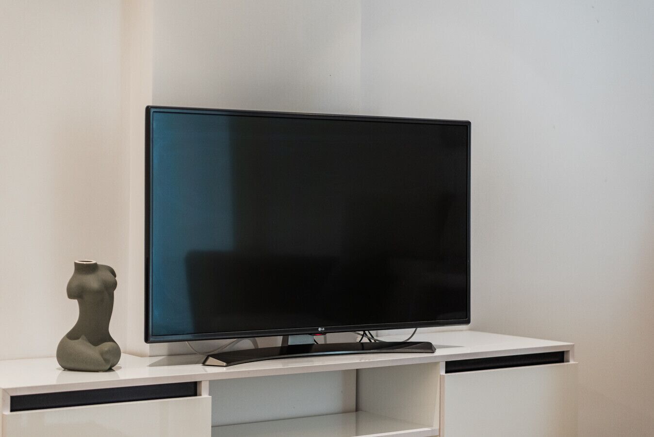 Een flatscreen-televisie op een witte tv-kast met een plank eronder.