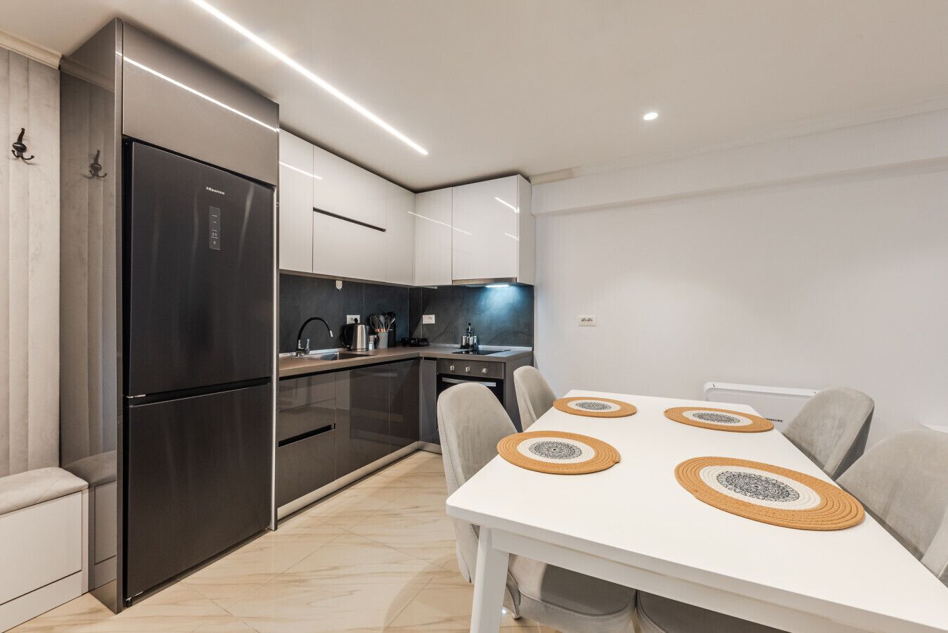Una cocina moderna con refrigerador, horno y microondas integrados. Hay una mesa de comedor con cuatro sillas y una encimera blanca.