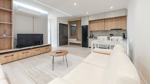 Una sala de estar moderna con un televisor de pantalla plana, un sofá, una mesa de centro y una zona de cocina con armarios de madera y un refrigerador.