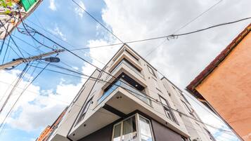 A modern building with a prominent corner balcony, multiple windows, and visible power lines against a partly cloudy sky.