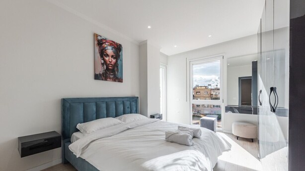 Un dormitorio moderno con una cama grande, un cuadro en la pared y vistas de la ciudad a través de la ventana.