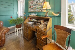 A room with teal walls, a wooden desk with drawers, a wicker chair, and a potted plant.
