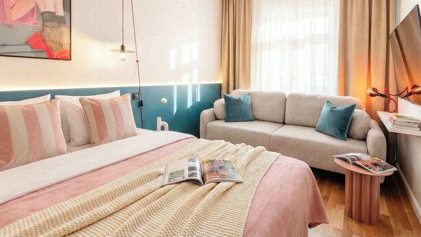 A hotel room with a bed, a sofa, a small side table, a lamp, and a painting on the wall.