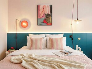 A neatly made bed with a teal headboard, a single red apple, and a book on a bedside table.