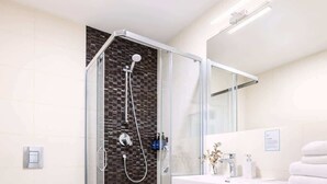 A modern bathroom with a glass-enclosed shower, a toilet, a sink with a mirror, and a front-loading washing machine.