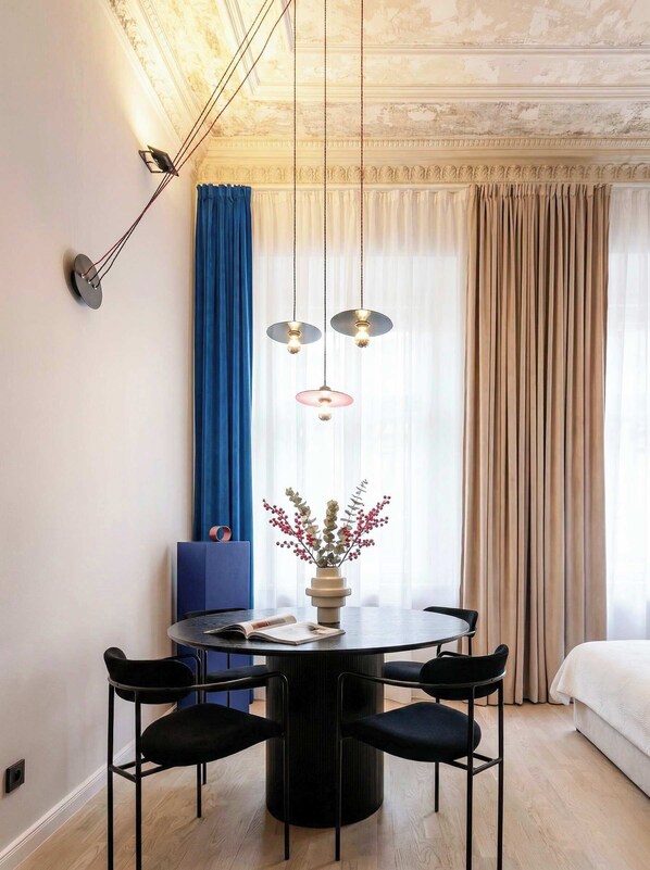 Et moderne hotelværelse med et rundt spisebord, fire stole, en vase med blomster og en seng.