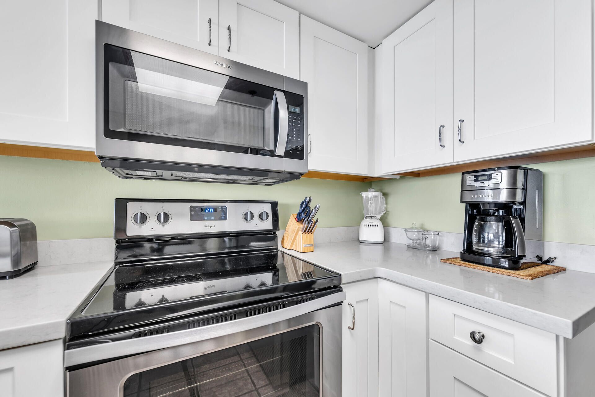 A modern kitchen with white cabinets, a stainless steel microwave, a built-in oven, a coffee maker, and a knife block.