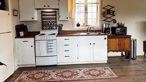 Una cocina compacta con armarios blancos, estufa, pileta y cafetera.