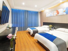 Habitación de hotel con dos camas, un escritorio, un televisor y un ventanal grande con cortinas azules.