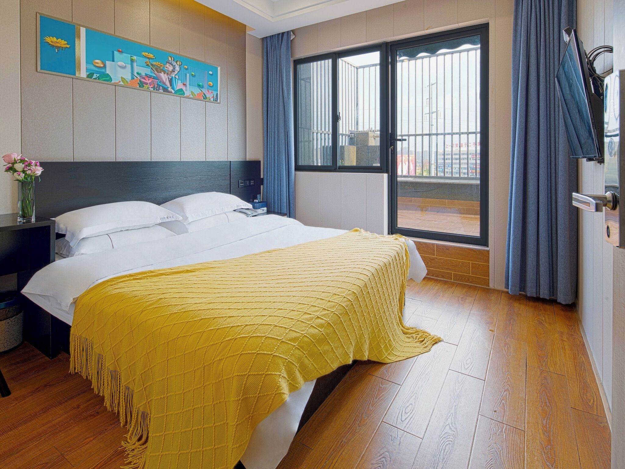 Een hotelkamer met een bed, een nachtkastje, een schilderij aan de muur en uitzicht door het raam.