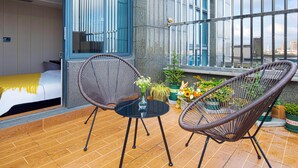 A modern room with a bed, two wicker chairs, a small table with a vase, and a balcony with potted plants. - RC SMART HOTEL (Yancheng)