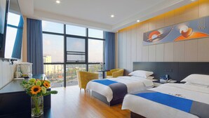 A hotel room with two beds, a desk with a vase of flowers, a chair, and a large window offering a city view. - RC SMART HOTEL (Yancheng)