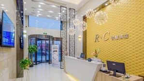 A hotel reception area with a modern design, featuring a reception desk, a digital screen, and a yellow textured wall. - RC SMART HOTEL (Yancheng)