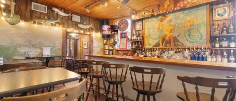 A restaurant interior with wooden furniture, a bar area, and a mural on the wall.
