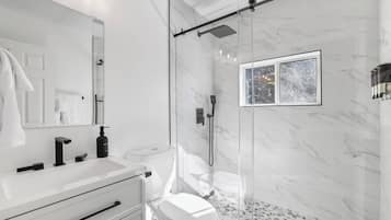 A modern bathroom with a glass-enclosed shower, a white sink, and a toilet.