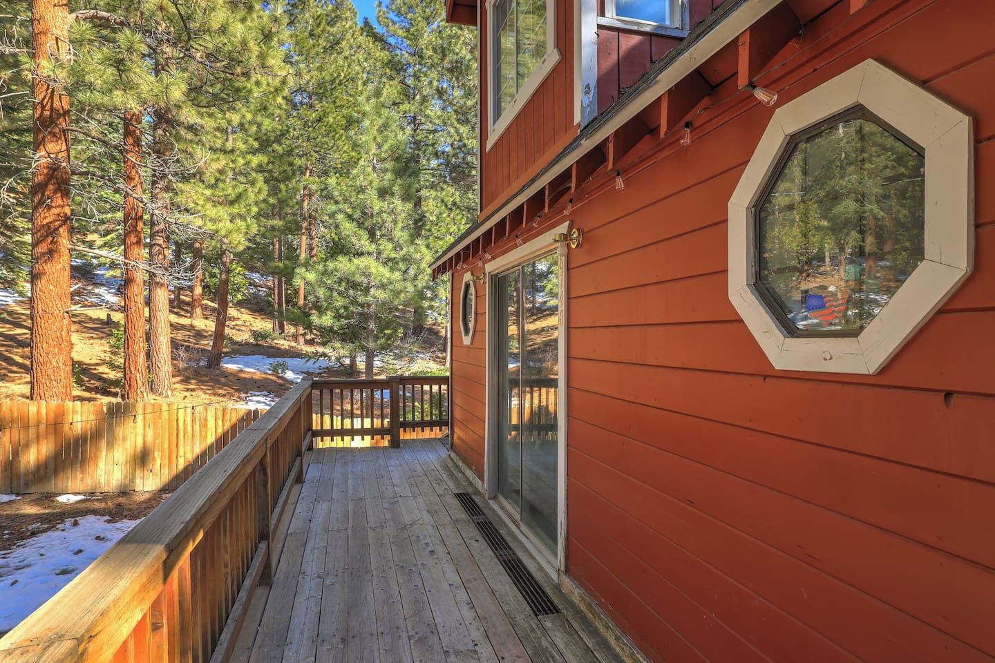 A wooden deck with a glass door leading to a room, surrounded by a forest.