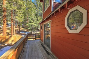 A wooden deck with a glass door leading to a room, surrounded by a forest.