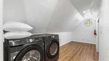 Una lavandería con dos lavadoras Samsung, una pared blanca, suelo de madera y un extintor en la pared.