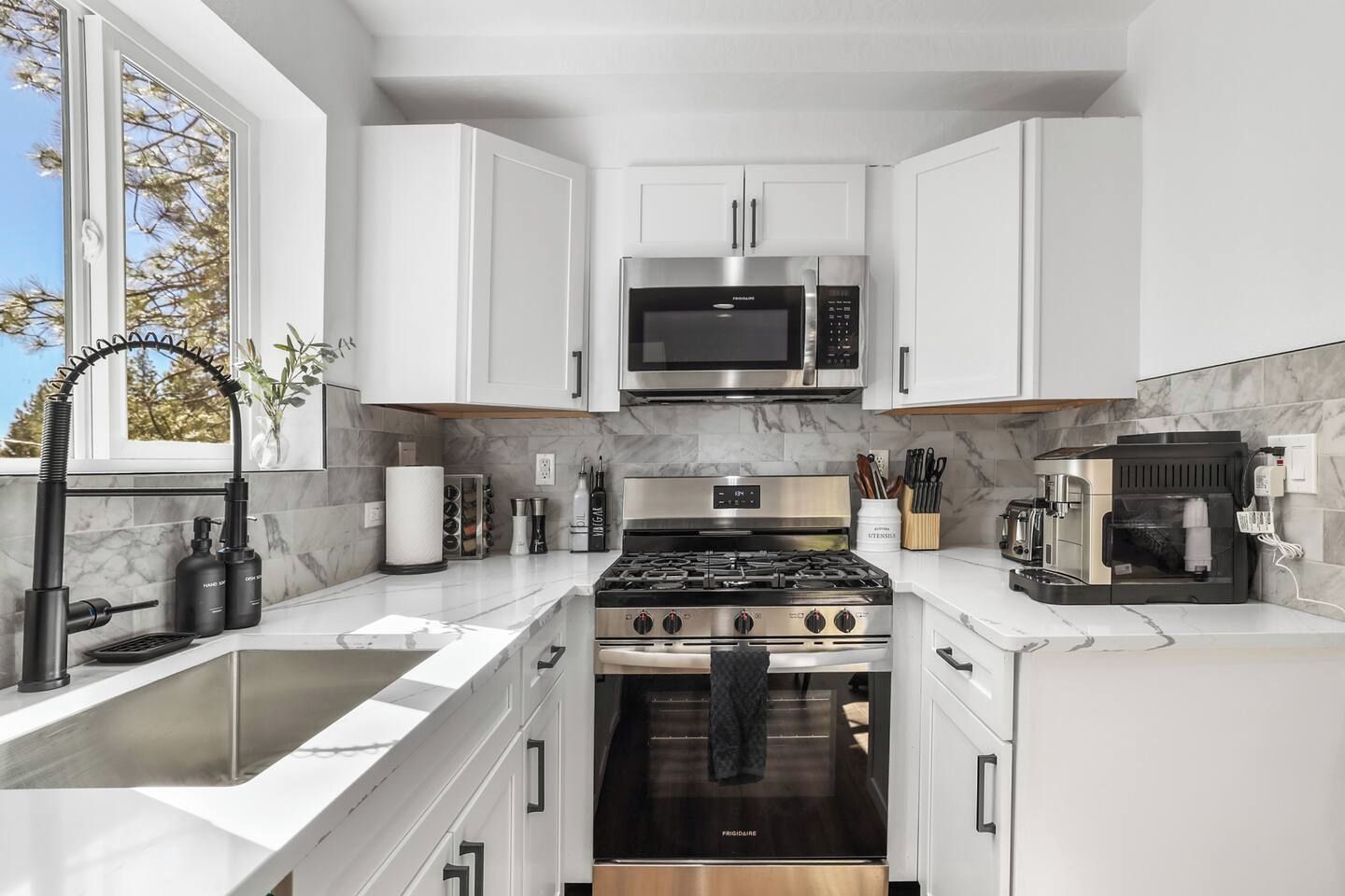 A modern kitchen with white cabinetry, a stainless steel stove, a microwave, and a coffee machine.