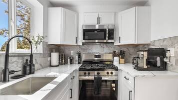 A modern kitchen with white cabinetry, a stainless steel stove, a microwave, and a coffee machine.