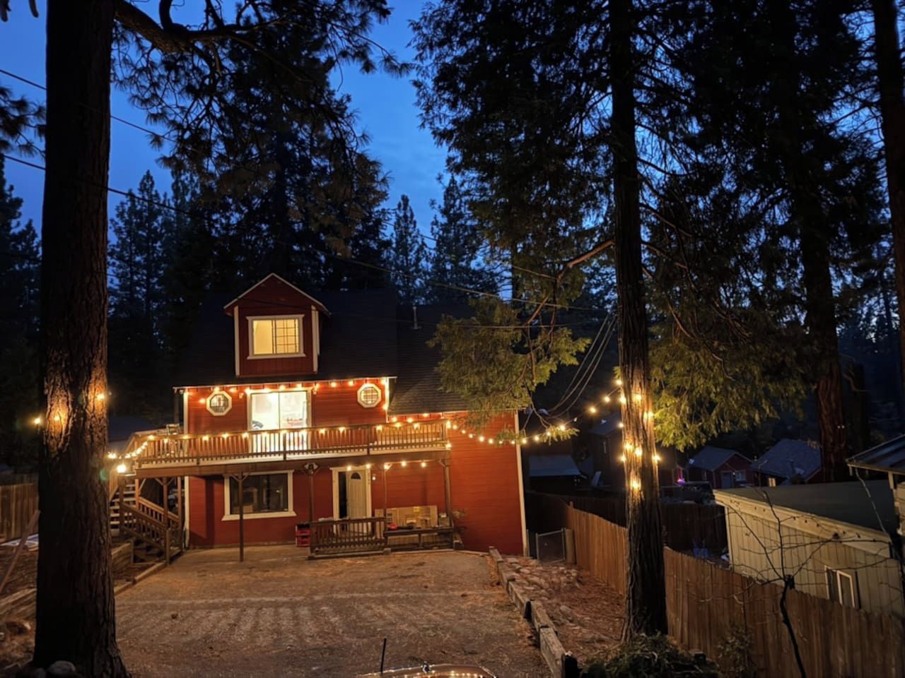 A two-story building with a balcony, surrounded by trees, and decorated with string lights.