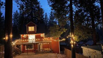 A two-story building with a balcony, surrounded by trees, and decorated with string lights.