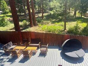 Een houten terras met tuinmeubilair, waaronder een bank, stoelen en een tafel.