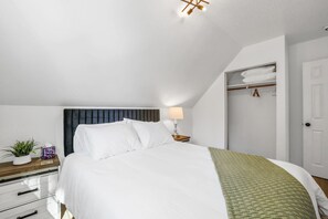 Une chambre à coucher avec un lit, une table de chevet, une lampe et une armoire où sont suspendus des vêtements.