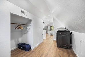 A narrow hallway with a wooden floor, a coat rack with hangers, a suitcase, and a radiator.