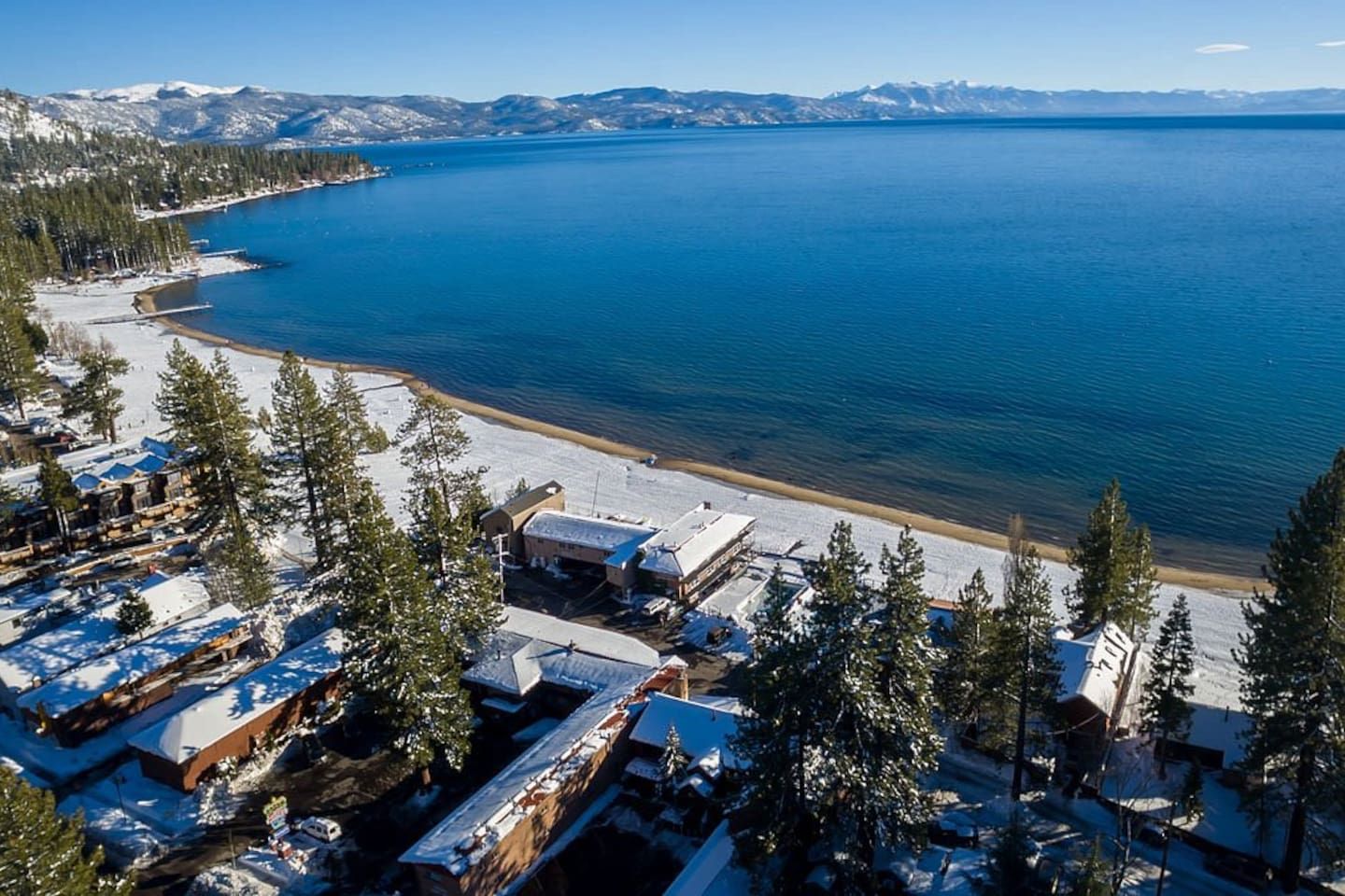 A coastal area with snow-covered buildings, a beach, and a clear view of the water.