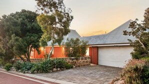 A residential house with a garage, surrounded by a landscaped garden with various plants and trees. - North Fremantle Retreat | Walk to Beach, River & Train (North Fremantle)