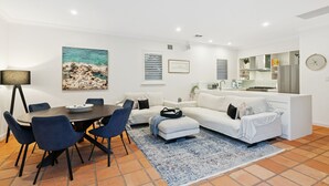 A modern living room with a dining area, white sofas, a coffee table, and a kitchen area with a stove and refrigerator. - North Fremantle Retreat | Walk to Beach, River & Train (North Fremantle)