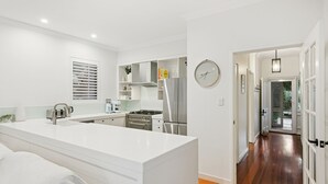 A modern kitchen with white cabinetry, a built-in oven, and a stainless steel refrigerator. - North Fremantle Retreat | Walk to Beach, River & Train (North Fremantle)